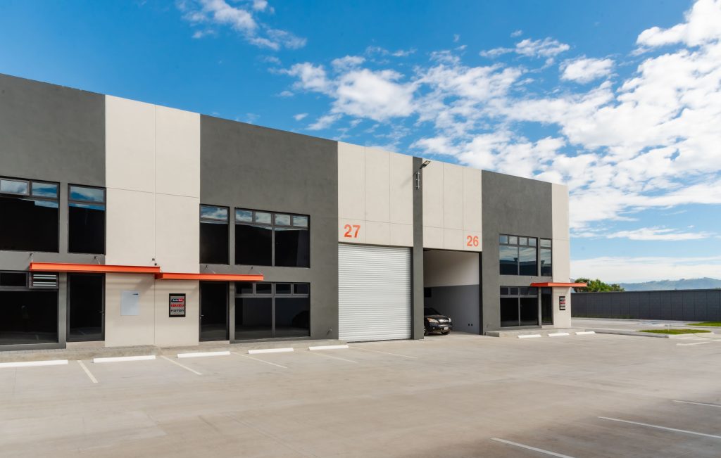 Modern gray and white industrial building with bay doors numbered 27 and 26 beneath a blue partly cloudy sky