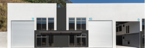 White industrial building with three large bay doors 11 10 9 and a central black storefront with glass windowshttps