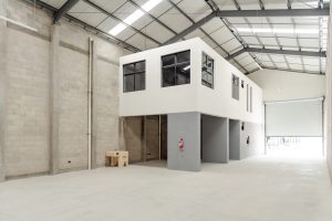 Spacious warehouse interior with a white two story office block gray walls and a large roll up door at the far end