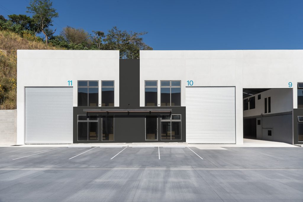 Modern industrial building with white façade labeled units 11 10 and 9 featuring two large roll up doors and a glass storefront in the center