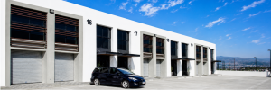 Modern white commercial building with numbered bays 1620 and metal shutter doors a black minivan parked in front under a blue sky