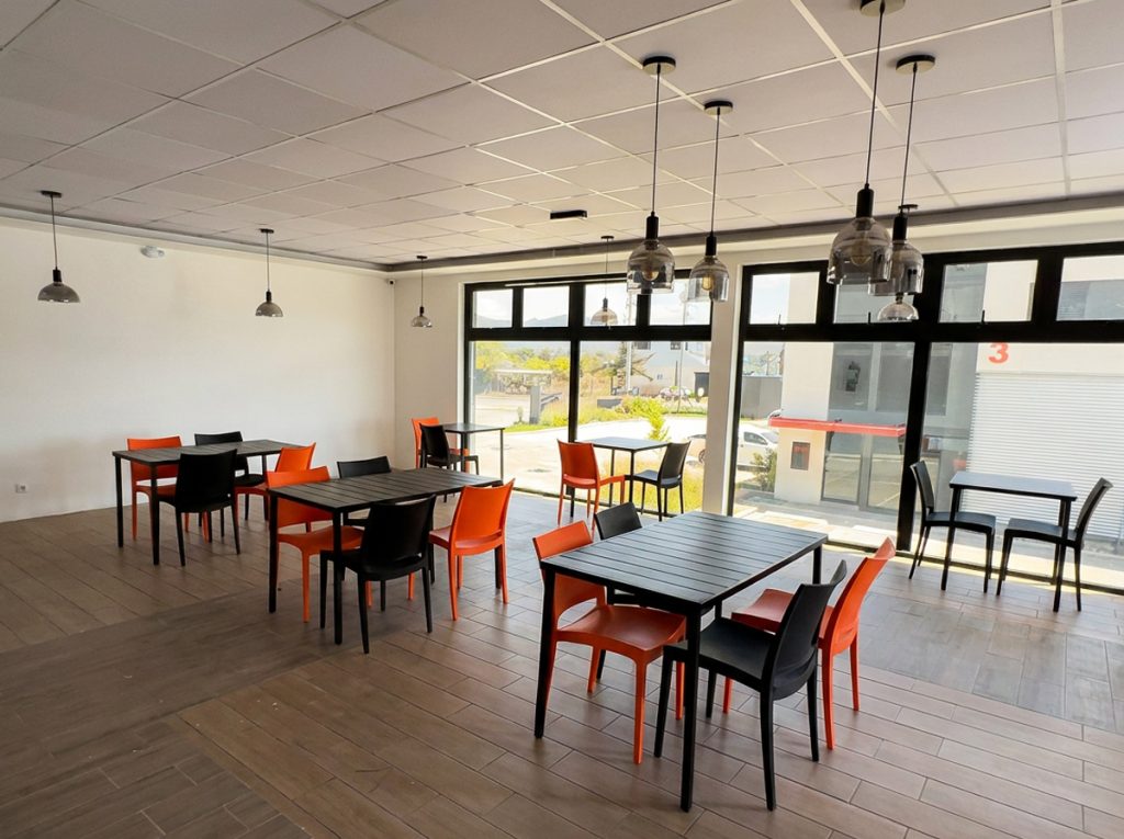 Bright cafe interior with dark wood tables and orange and black chairs large front windows and hanging pendant lights
